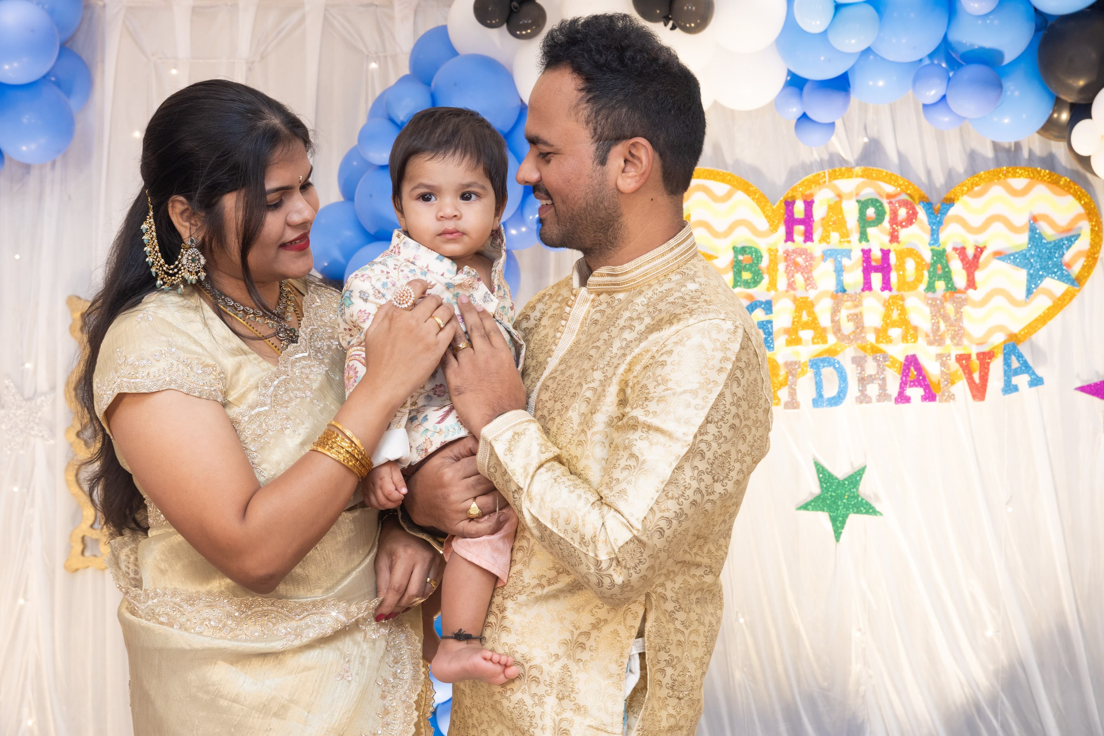 Parents holding child at birthday celebration with colorful backdrop