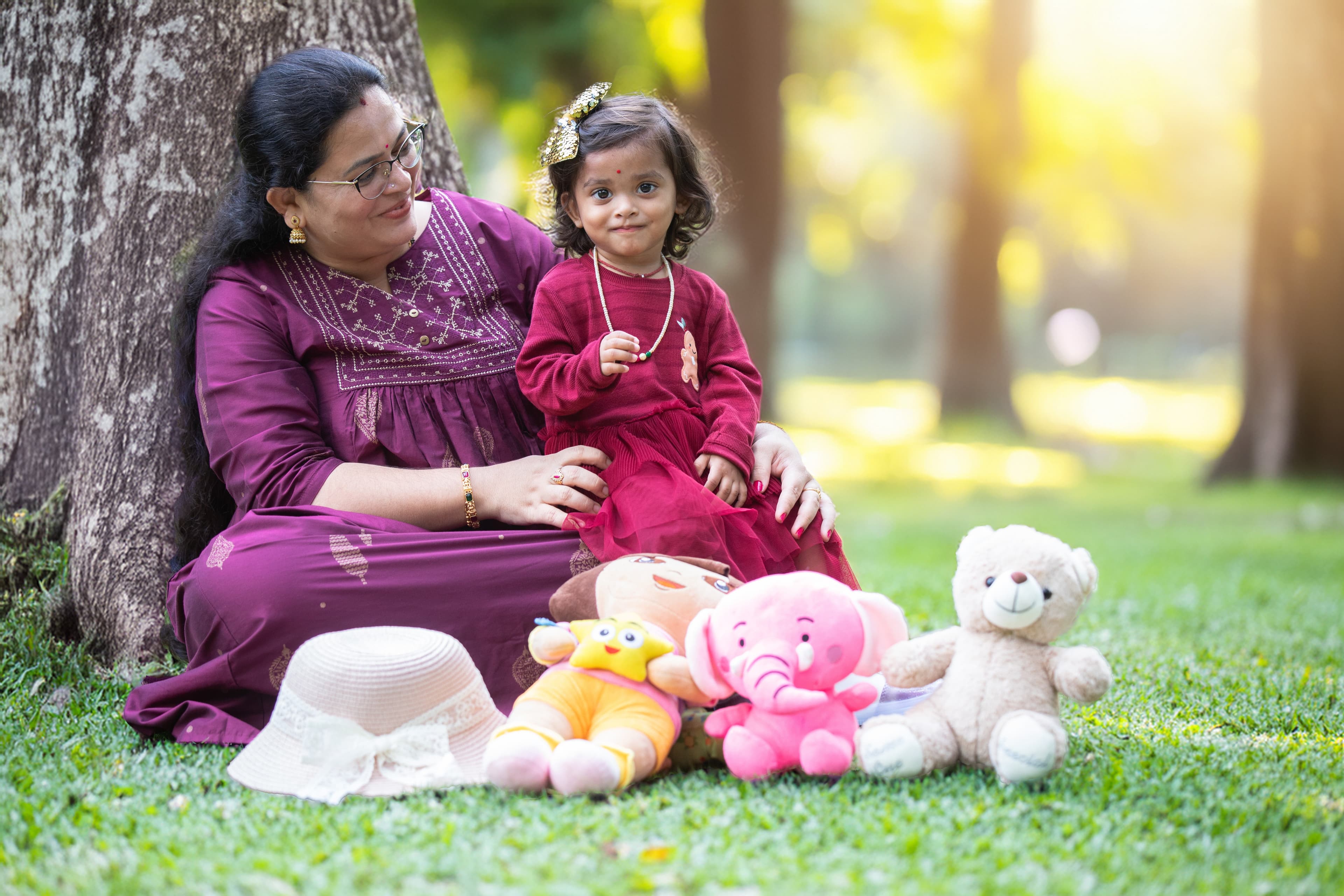 Mother and daughter sitting against tree with stuffed toys