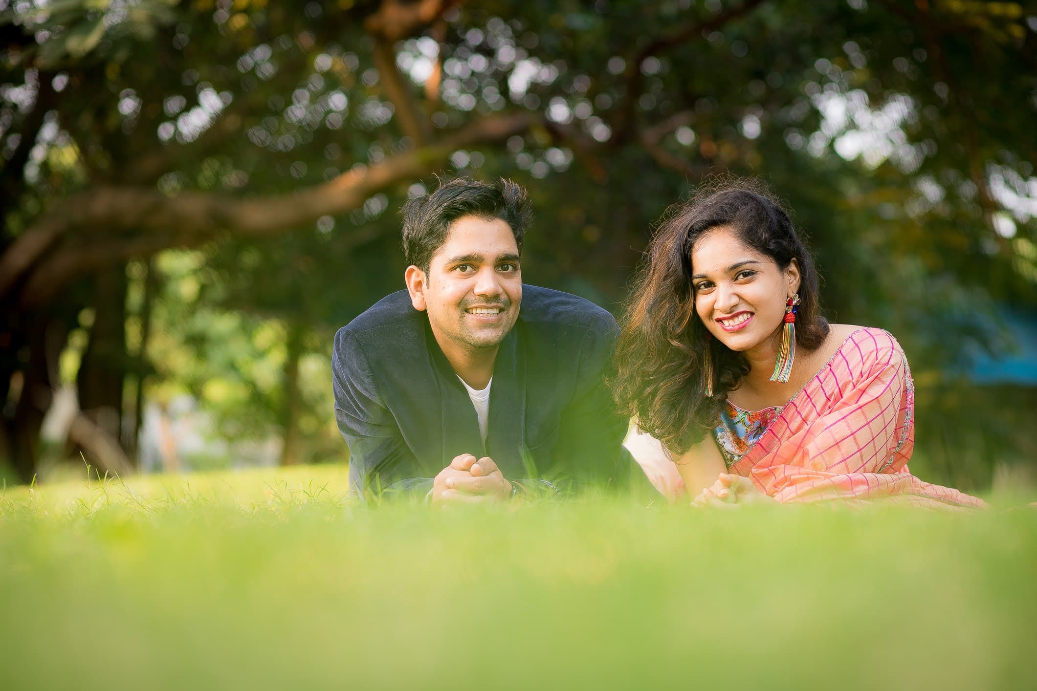 Couple lying on grass under leafy trees