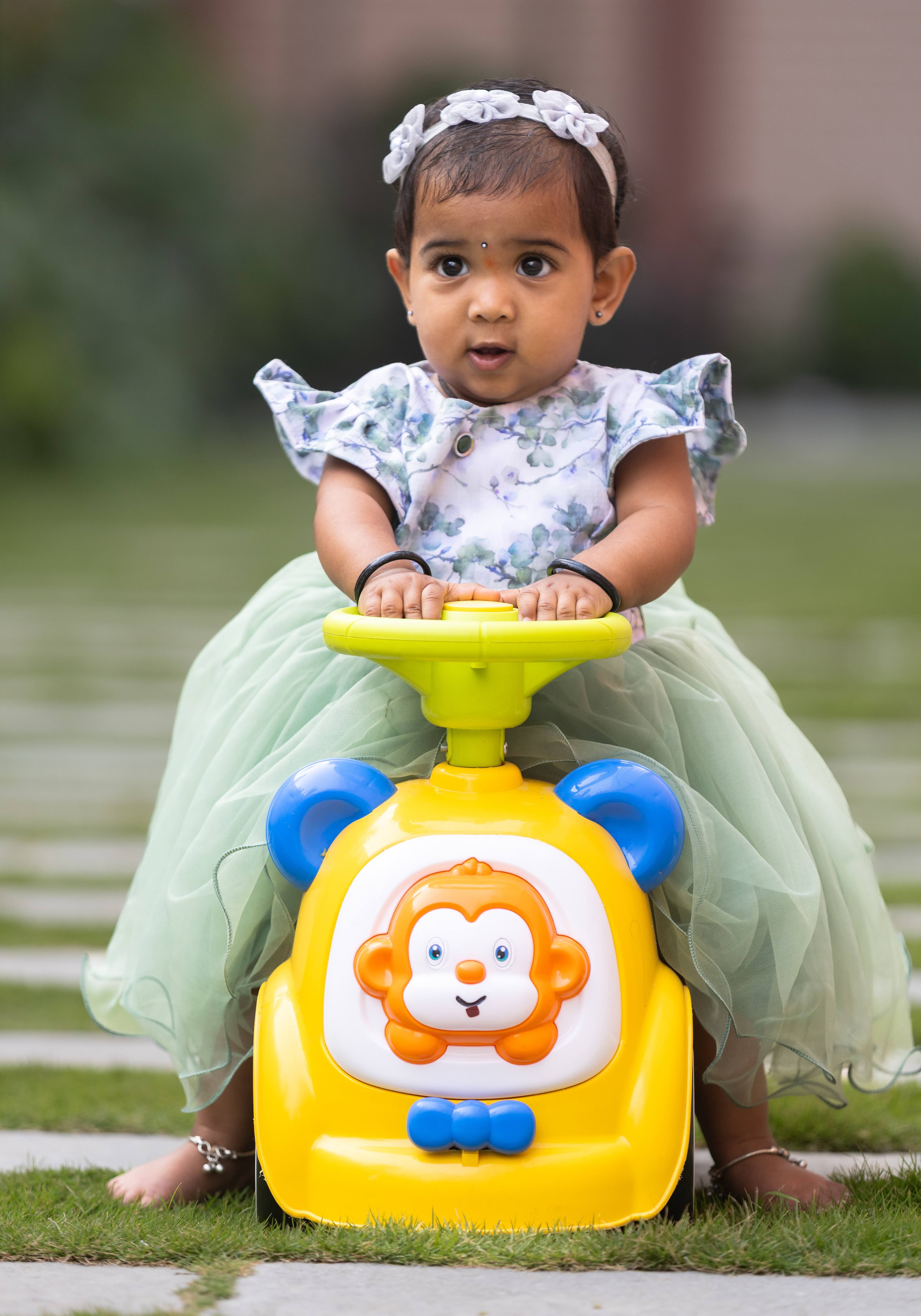 Toddler girl on yellow toy ride with white flower headband